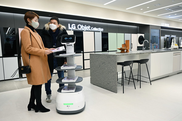 LGE 서초본점 LG 클로이 서브봇: LG베스트샵 서초본점을 방문한 고객들이 LG 클로이 서브봇이 가져다주는 안내책자를 살펴보고 있다.